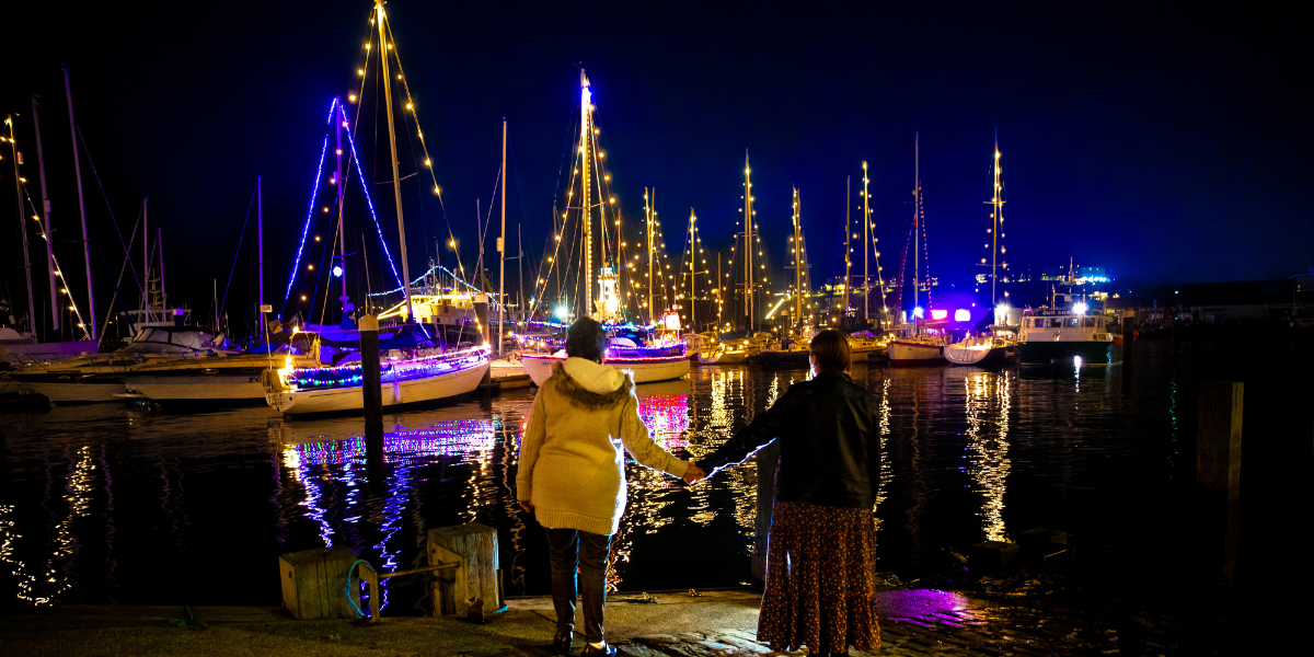 Two ladies hold hands in front of illuminated boats at Scarborough Harbour